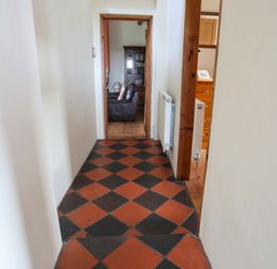 A hallway with black and red tiled floor leading to a room with a brown leather sofa and wooden furniture at Penrallt Fawr in Rhosgadfan near Waunfawr