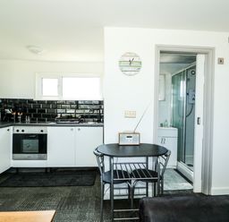A kitchen with black tiled backsplash a black dining table with two chairs and a bathroom visible at 57 Cherry Park Chapel St Leonards