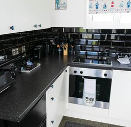 A kitchen with black countertop and backsplash white cabinets microwave oven stove and utensils at 57 Cherry Park in Chapel St Leonards
