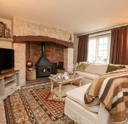A living room with a stone fireplace wood stove sofas curtains and a coffee table at Norden House in Maiden Newton