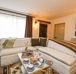 A living room with a white corner sofa and a coffee table set with tea cups and muffins at Norden House in Maiden Newton