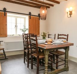 A dining room with a wooden table set for four near a window with wooden shutters at Norden House in Maiden Newton