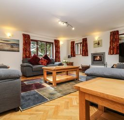 A living room with gray sofas red cushions a wooden coffee table fireplace and patterned curtains at South Boduel Farmhouse in Liskeard