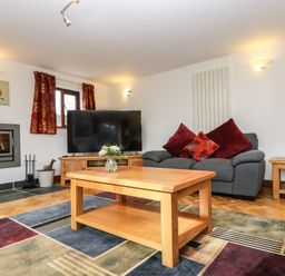 A living room with a sofa cushions wooden coffee table fireplace and television at South Boduel Farmhouse in Liskeard