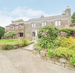 A stone farmhouse with a garden and flower beds in front at South Boduel Farmhouse in Liskeard