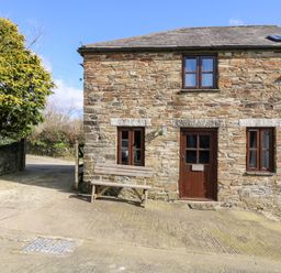 A stone cottage with wooden door and windows and a bench outside at Keepers Cottage in Liskeard