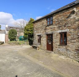 Exterior of a stone house with wooden door and windows a bench outside and other houses in the background at Keepers Cottage in Liskeard