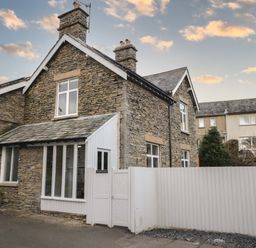 A stone house with white framed windows and a white fence at Raybarrow in Windermere