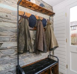 A hallway with coats and hats hanging on hooks and a bench below near a door at Raybarrow in Windermere