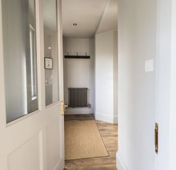 A hallway with a partially open door a wall radiator a coat rack and a floor mat at Raybarrow in Windermere