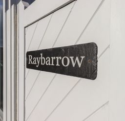 A black sign with white text reading Raybarrow on a white wooden surface at Raybarrow in Windermere