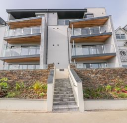 The front view of a modern apartment building with balconies stone walls and a central staircase at Onshore in Newquay