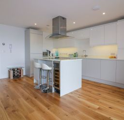 A modern kitchen with white cabinets a kitchen island with two stools and wood flooring at Onshore in Newquay