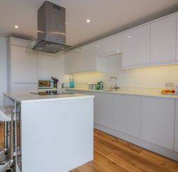 A modern kitchen with white cabinets a kitchen island with stools and wooden flooring at Onshore in Newquay