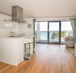 A kitchen and living area with breakfast bar stools and a balcony overlooking the sea at Onshore in Newquay