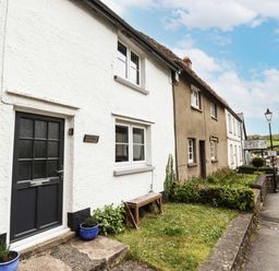 A row of cottages along a street with a small garden and bench outside Lavender Cottage in South Zeal