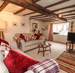 A living room with two sofas red and plaid cushions a wooden coffee table a floor lamp a television on a stand striped rug and exposed wooden ceiling beams at Lavender Cottage in South Zeal