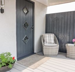 A porch with a gray door a wicker chair with cushion and small table with flowers at Westfields Kennards House near Launceston