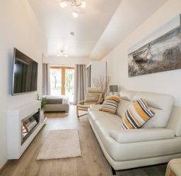 A living room with a white sofa with striped cushions a white fireplace and a wall mounted TV at Westfields Kennards House near Launceston