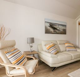 A living room with a beige sofa and chair with striped cushions a wooden side table with a lamp and a painting of a boat on the wall at Westfields in Kennards House near Launceston