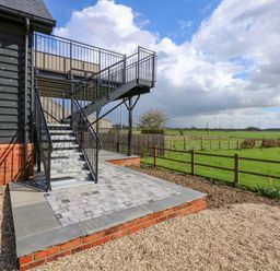 Metal staircase leading to an elevated patio beside a building with a gravel and paved patio area and a view of fenced green fields at The Attic in Blackborough End near King's Lynn
