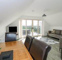 A dining table with chairs a gray sofa a small table and a TV in a living room with glass doors opening to a balcony at The Attic in Blackborough End near Kings Lynn