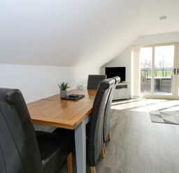 A dining table with black chairs and a small plant beside sliding glass doors with a view of a balcony and greenery at The Attic in Blackborough End near King's Lynn