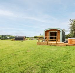 Two wooden pods on a grassy field with outdoor seating and a hot tub at Hwyl Rhayader near Llandrindod Wells