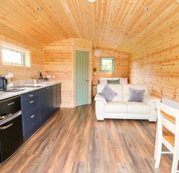 A wooden cabin interior with a kitchen counter sofa bed and dining table at Hwyl in Rhayader near Llandrindod Wells
