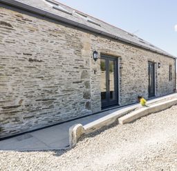 Exterior of a stone building with two black framed glass doors and small plants in pots at The Cornstore in Helland near Bodmin