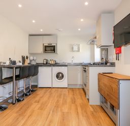 A kitchen with bar stools a washing machine and a wall mounted television at The Cornstore in Helland near Bodmin