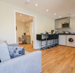 A living room with a grey sofa and black bar stools at a kitchen counter and wood flooring at The Cornstore in Helland near Bodmin