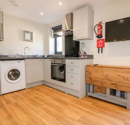 A kitchen with washing machine oven microwave wooden folding table and wall mounted television at The Cornstore in Helland near Bodmin