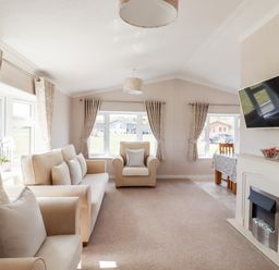 A living room with beige sofas curtains and a wall-mounted TV at 12 Bucklesham Park in Bucklesham near Trimley St Martin