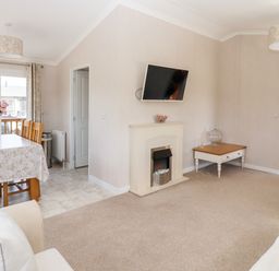 A living room with a fireplace a wall mounted tv a dining table with flowers and chairs at 12 Bucklesham Park in Bucklesham near Trimley St Martin