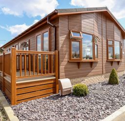 A wooden mobile home with a small porch and gravel landscaping at 12 Bucklesham Park in Bucklesham near Trimley St Martin
