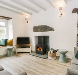 A living room with a wood burning stove two sofas a TV on a stand window seat with cushions and built in shelves at Turn Cottage in Satterthwaite near Hawkshead