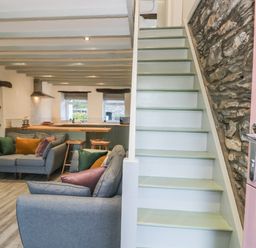 A living room with gray sofas and colorful cushions next to stairs and an open kitchen at Turn Cottage in Satterthwaite near Hawkshead
