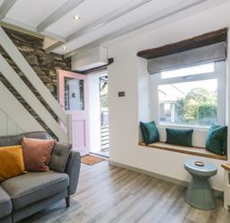 A living room with a gray sofa cushions a pink door window seat with cushions a small blue stool and a television at Turn Cottage in Satterthwaite near Hawkshead