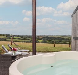 An outdoor area with a hot tub and chairs overlooking the countryside at The Pennymoor in Cadeleigh near Tiverton