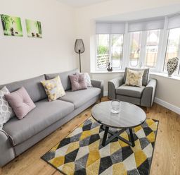 A living room with gray sofa and armchair yellow and gray rug and round coffee table at Globe Cottage in Stratford-Upon-Avon