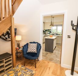 An entrance area with a wooden staircase a blue chair with a pillow a side table with a lamp and a door leading to a kitchen at Globe Cottage in Stratford-Upon-Avon