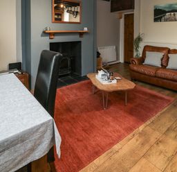 A living room with a brown leather sofa a wooden coffee table and a red rug at Maple Tree Cottage in Longframlington
