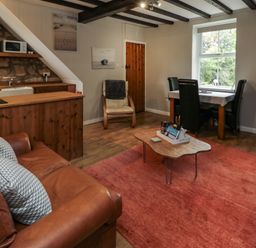 A living room with a brown leather sofa a wooden coffee table a dining table with black chairs and a wooden kitchen area at Maple Tree Cottage in Longframlington