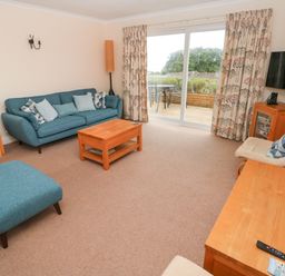 A living room with blue sofa chairs wooden tables and a TV by sliding glass doors at Trem Y Morfa in Newport Pembrokeshire