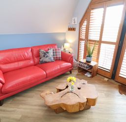 A living room with a red sofa wooden coffee table and window shutters at Silver Birch Lodge in Misterton
