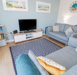 A living room with two blue sofas a patterned rug a TV on a cabinet and bookshelves at 14 Parc Delfryn Brynteg near Benllech