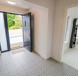An entryway with an open black door and patterned tile floor leading to a room with a chair bookshelf and floor lamp at Wee Andy's in Slavary near Buncrana County Donegal