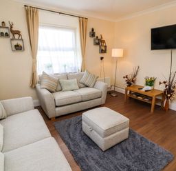 A living room with two sofas a footstool a rug a coffee table a wall-mounted television and decorative shelves at Neland View in Windermere