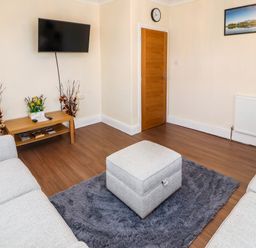 A living room with two sofas a gray ottoman on a gray rug a wall mounted television a wooden table with decorations and a wooden door at Neland View in Windermere